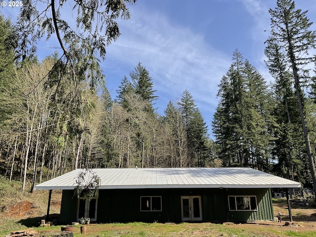 exterior space with metal roof, a view of trees, french doors, and board and batten siding