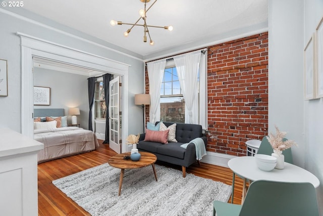 living room with a notable chandelier, light hardwood / wood-style flooring, ornamental molding, and brick wall