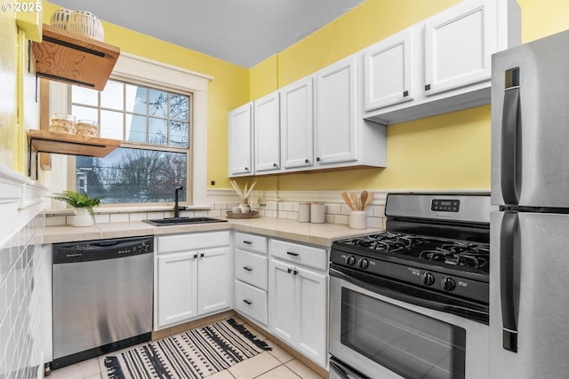 kitchen featuring sink, light tile patterned floors, appliances with stainless steel finishes, white cabinetry, and tile counters