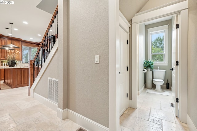corridor with stone tile floors, plenty of natural light, recessed lighting, stairway, and baseboards