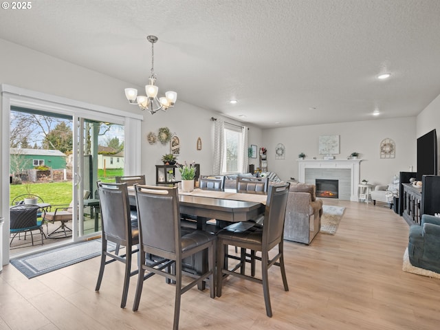 dining area featuring a chandelier, a glass covered fireplace, a textured ceiling, and light wood-type flooring