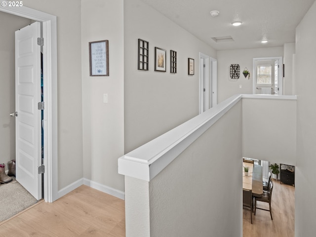 corridor with an upstairs landing, baseboards, and wood finished floors