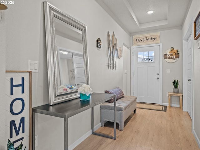 foyer entrance with baseboards, a raised ceiling, and light wood-style flooring