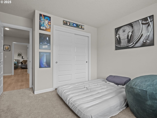 bedroom with light colored carpet, baseboards, a closet, and a textured ceiling