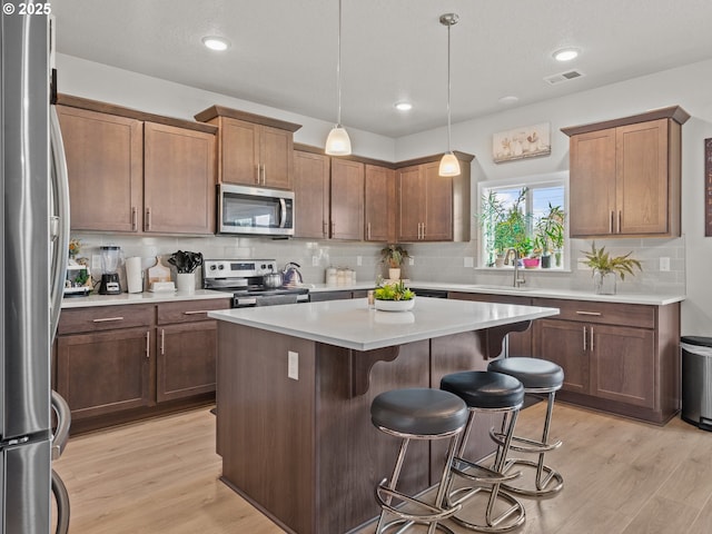 kitchen featuring a kitchen island, a breakfast bar, light wood-type flooring, stainless steel appliances, and a sink