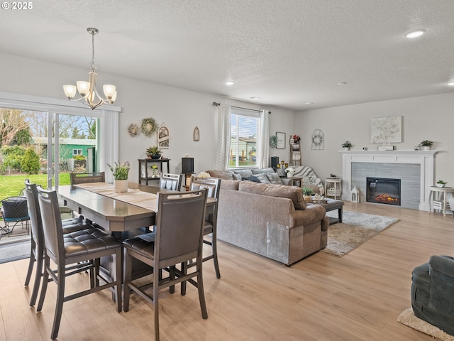 dining area featuring light wood-style flooring, a notable chandelier, a fireplace, and a textured ceiling