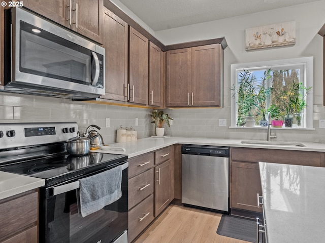 kitchen with a sink, decorative backsplash, light wood-type flooring, and appliances with stainless steel finishes