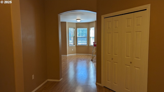 hall featuring arched walkways, baseboards, and wood finished floors