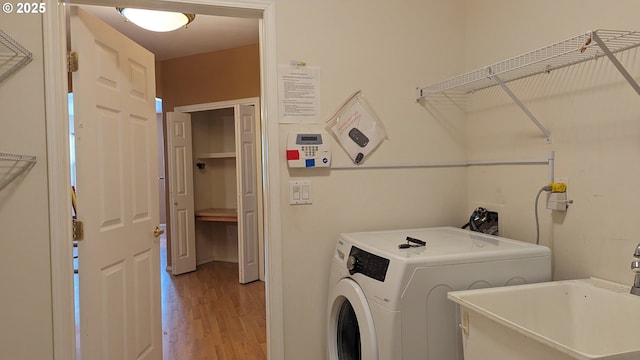 laundry room featuring laundry area, washing machine and dryer, a sink, and light wood-style flooring