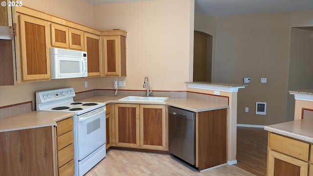 kitchen with a sink, light wood finished floors, white appliances, light countertops, and a peninsula