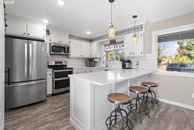 kitchen featuring decorative backsplash, a peninsula, wood finished floors, and appliances with stainless steel finishes