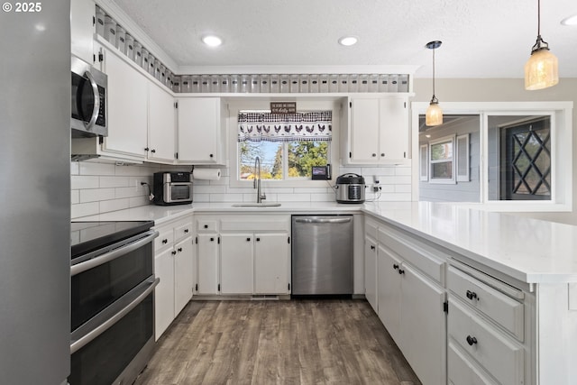 kitchen featuring dark wood-style floors, a peninsula, a sink, stainless steel appliances, and tasteful backsplash