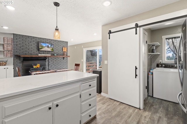 kitchen featuring a textured ceiling, white cabinetry, a barn door, light wood-style floors, and light countertops