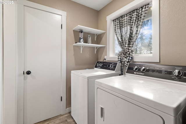 clothes washing area featuring laundry area, separate washer and dryer, light wood-type flooring, and a textured wall