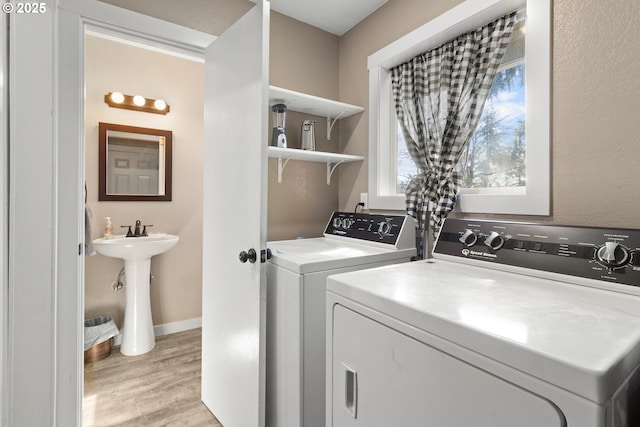 clothes washing area featuring laundry area, baseboards, light wood-type flooring, and washer and clothes dryer