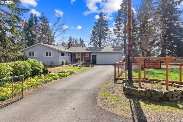 ranch-style house with fence, aphalt driveway, roof mounted solar panels, a chimney, and an attached garage