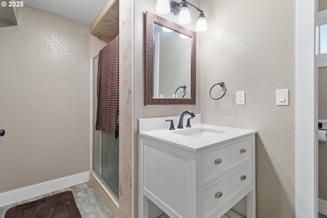 bathroom featuring a shower stall, baseboards, wood finished floors, a textured wall, and vanity