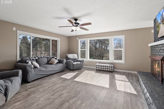 living room with a fireplace, a textured ceiling, ceiling fan, and wood finished floors