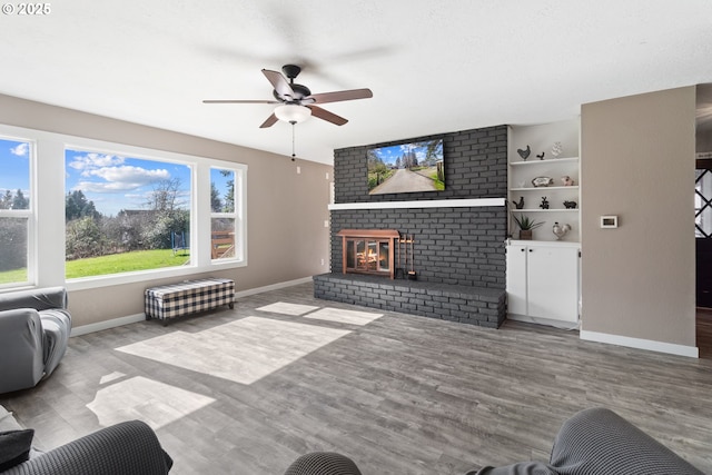 living area with baseboards, a brick fireplace, wood finished floors, and a ceiling fan