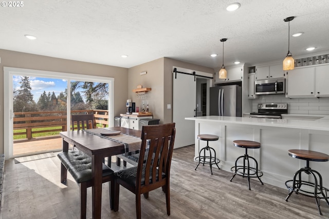 dining space featuring light wood finished floors, recessed lighting, a textured ceiling, and a barn door