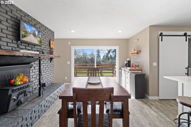 dining space featuring light wood-style flooring, a textured ceiling, a barn door, a fireplace, and baseboards