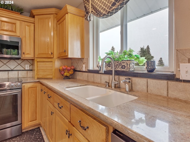 kitchen featuring light stone countertops, backsplash, stainless steel appliances, and sink