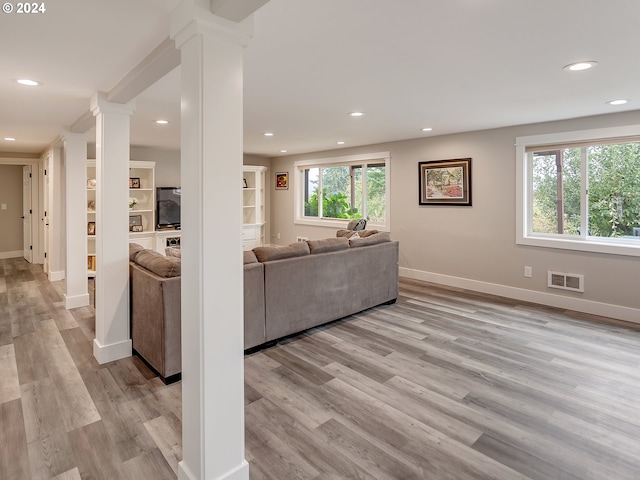 living room with light wood-type flooring, a wealth of natural light, and decorative columns