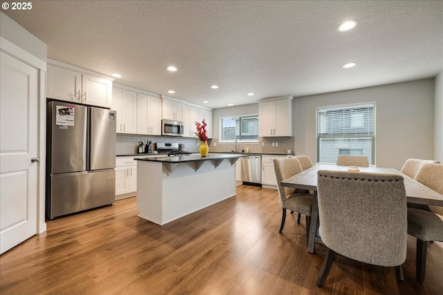 kitchen featuring a breakfast bar area, stainless steel appliances, wood finished floors, a kitchen island, and dark countertops