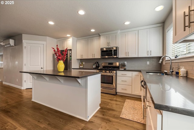 kitchen featuring a breakfast bar area, dark wood-type flooring, a sink, appliances with stainless steel finishes, and a wall mounted air conditioner