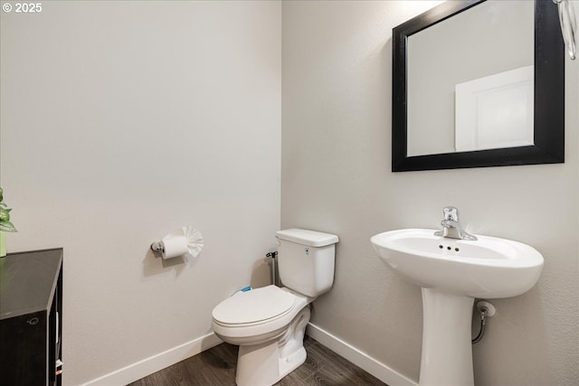 half bathroom with wood finished floors, toilet, and baseboards