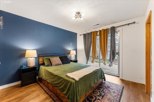 bedroom with a textured ceiling, wood finished floors, visible vents, and access to exterior