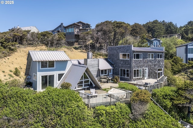 back of house featuring a wooden deck, metal roof, and a chimney