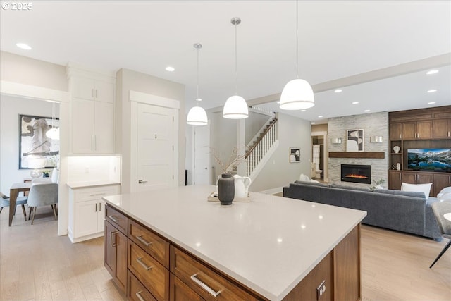 kitchen featuring a kitchen island, a fireplace, light wood-style floors, light countertops, and white cabinetry
