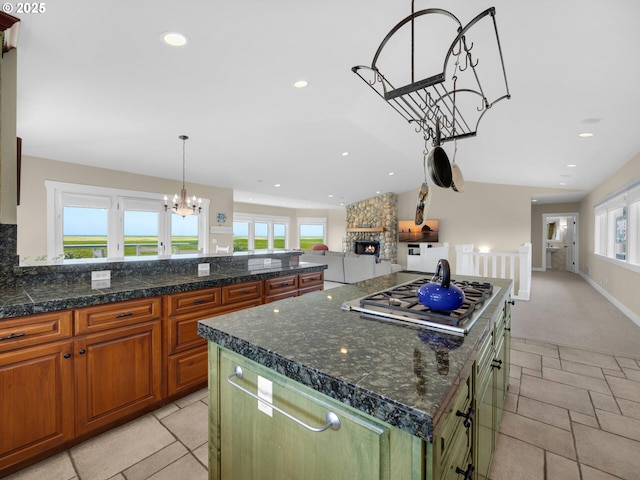 kitchen with stainless steel gas cooktop, a chandelier, a fireplace, open floor plan, and brown cabinetry
