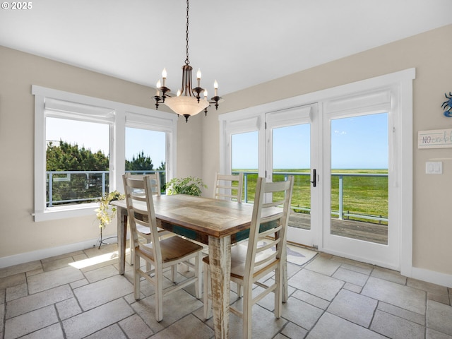 dining room featuring stone tile flooring, baseboards, and a chandelier