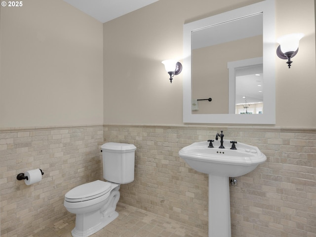 half bath featuring wainscoting, tile walls, and toilet