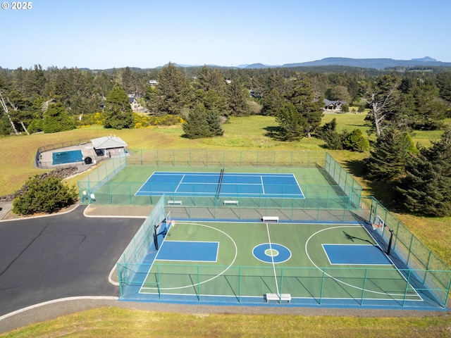 view of sport court with a tennis court, fence, a forest view, and a mountain view