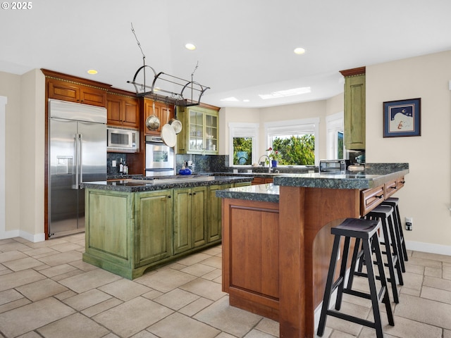 kitchen with built in appliances, recessed lighting, baseboards, tasteful backsplash, and a breakfast bar