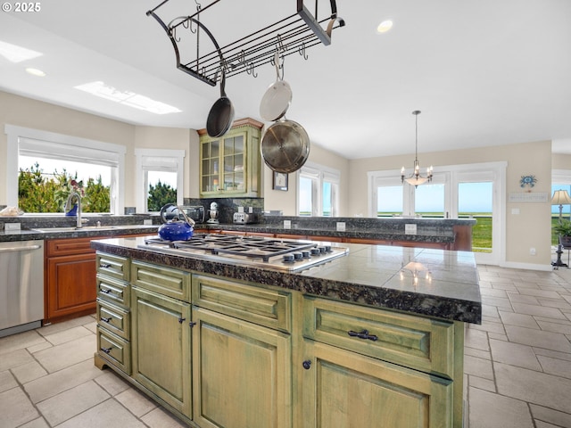 kitchen with a sink, stainless steel appliances, a kitchen island, glass insert cabinets, and tile countertops