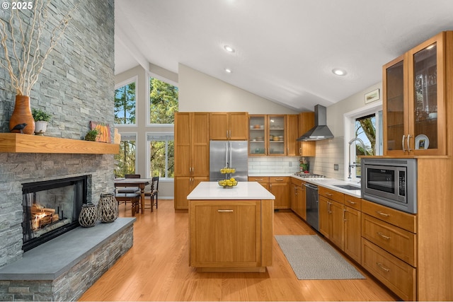 kitchen with light wood-style flooring, a sink, appliances with stainless steel finishes, wall chimney range hood, and a center island