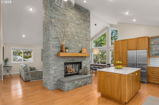 kitchen with light wood-style flooring, high end refrigerator, a kitchen island, a fireplace, and open floor plan