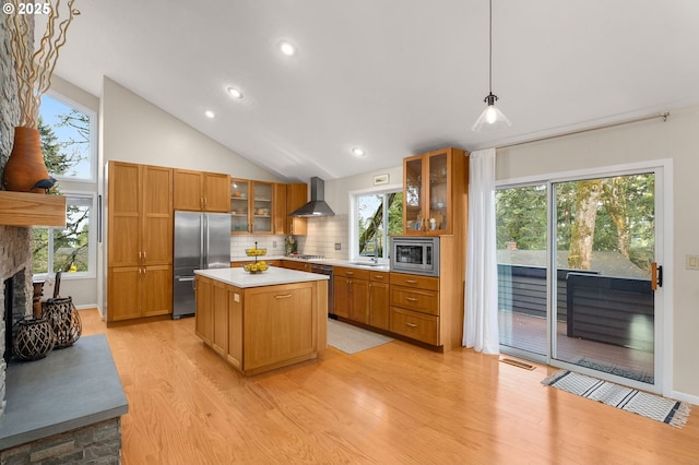 kitchen featuring built in appliances, a fireplace, light countertops, brown cabinets, and wall chimney exhaust hood