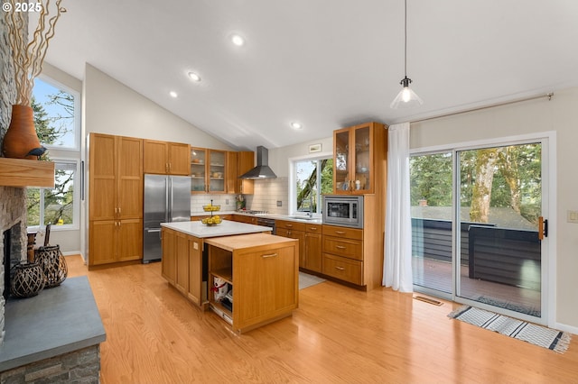 kitchen featuring built in appliances, a fireplace, a kitchen island, wall chimney range hood, and brown cabinetry