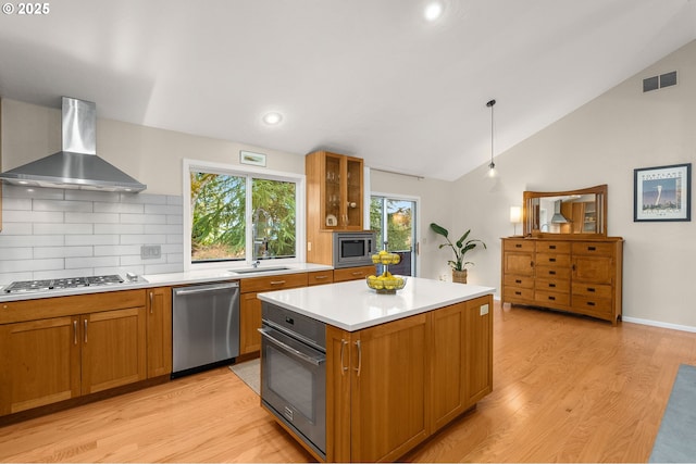 kitchen featuring lofted ceiling, stainless steel appliances, a sink, visible vents, and wall chimney exhaust hood