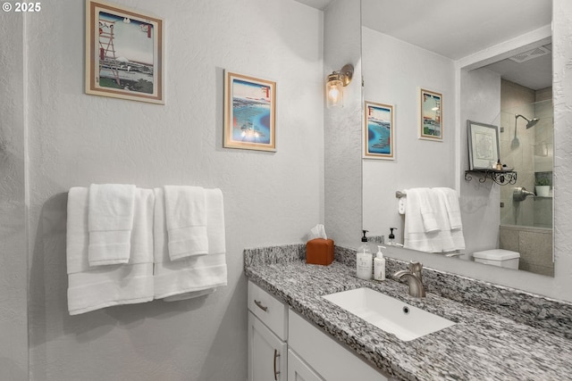 full bath with visible vents, tiled shower, a textured wall, and vanity