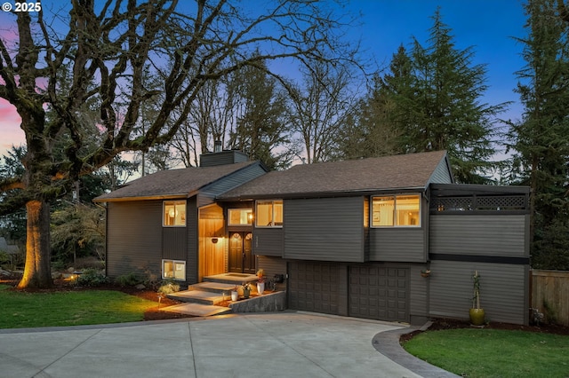 view of front of property featuring a front lawn, concrete driveway, a chimney, and an attached garage