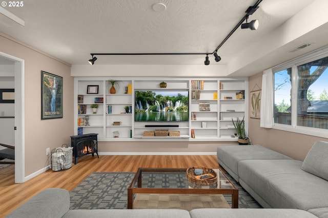 living area featuring visible vents, wood finished floors, a wood stove, rail lighting, and a textured ceiling