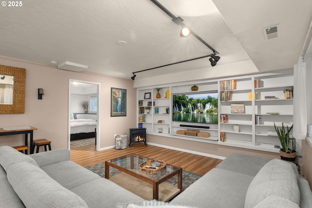 living area with a wood stove, visible vents, a textured ceiling, and wood finished floors