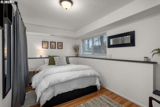 bedroom featuring visible vents, a textured ceiling, baseboards, and wood finished floors