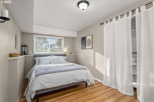 bedroom with a textured ceiling, wood finished floors, and baseboards